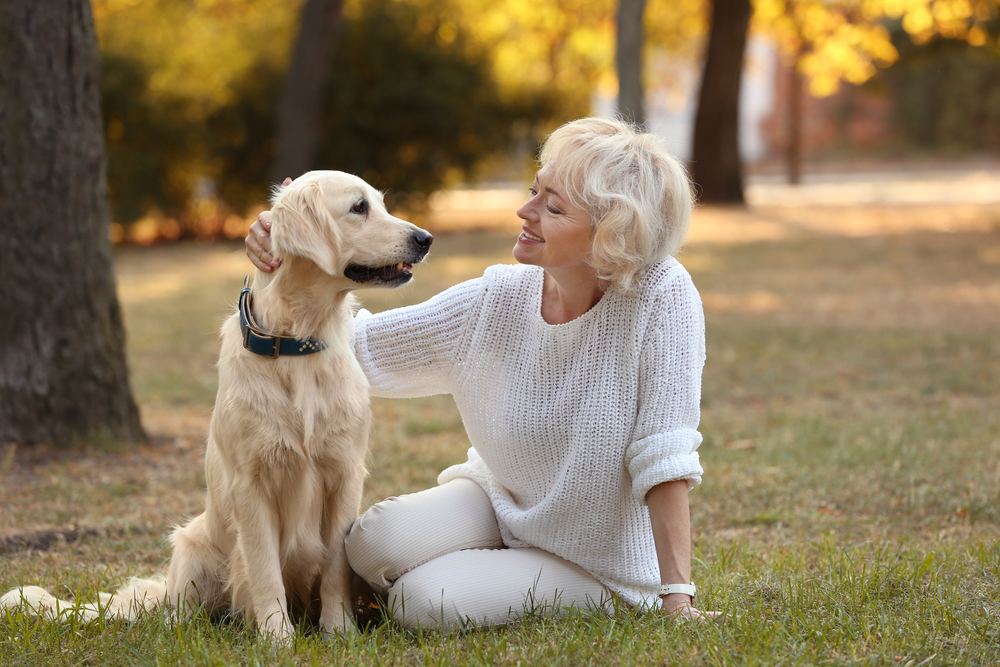 Senior woman sitting on grass in a park with her large dog, enjoying pet companionship