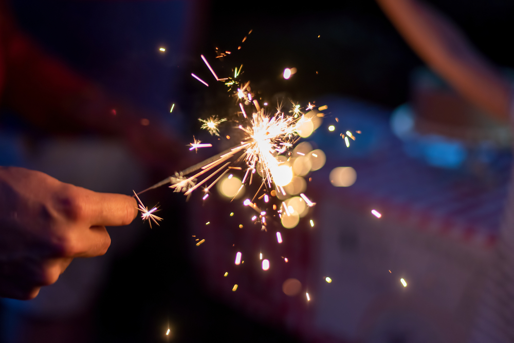 Hand holding a lit sparkler outdoors at dusk — pet fireworks safety tips