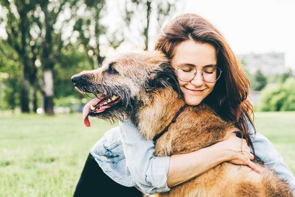 Happy woman hugging her dog outdoors in a summer park during pet wellness visit