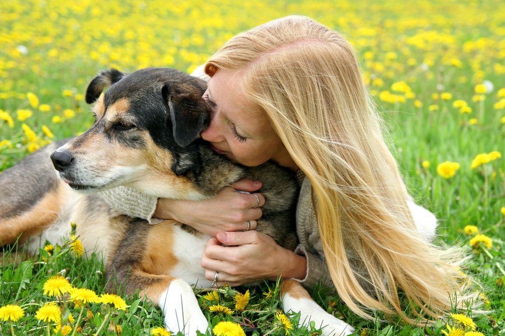 Young girl lying in the grass outdoors tenderly hugging her pet